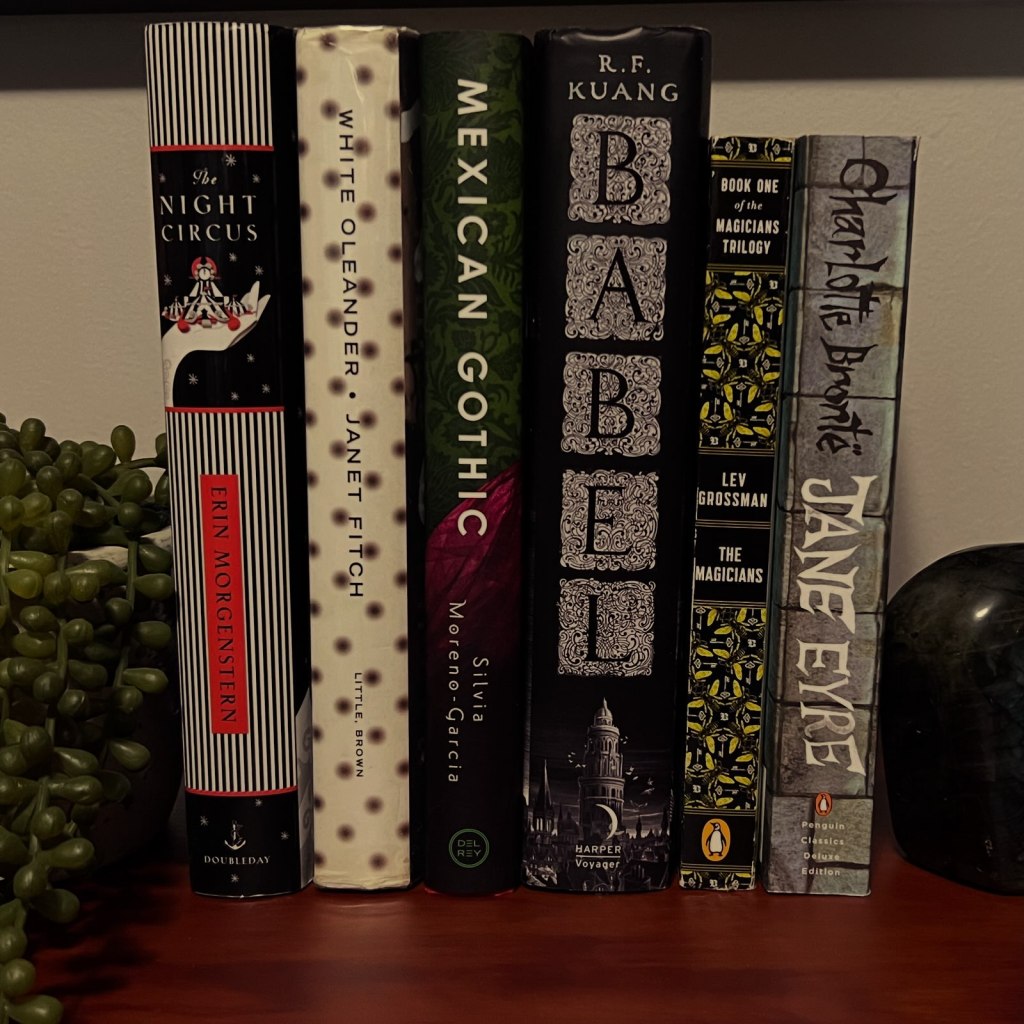 A picture of the spines of  six books side by side, from left o right: The Night Circus by Erin Morgenstern, White Oleander by Janet Fitch, Mexican Gothic by Silvia Moreno-Garcia, Babel by R. F. Kuang, The Magicians by Lev Grossman, and Jane Eyre by Charlotte Bronte